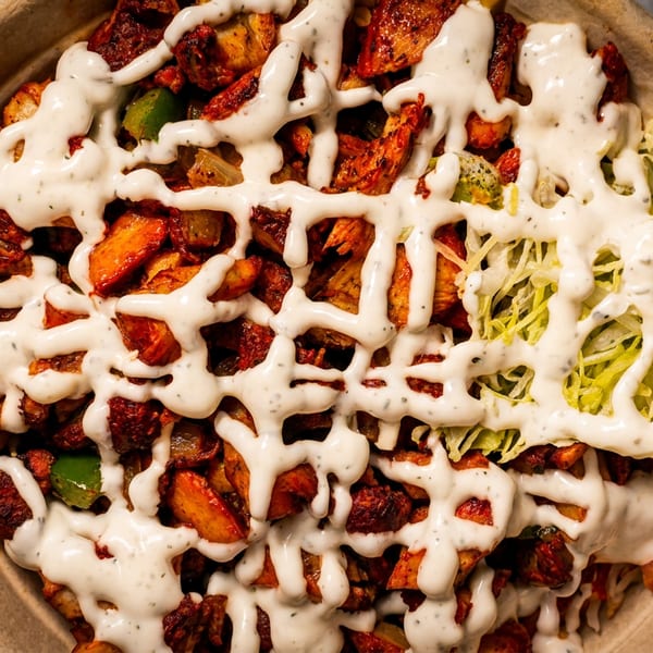 Overhead view of a bowl filled with chicken, potatoes, lettuce, and white sauce.